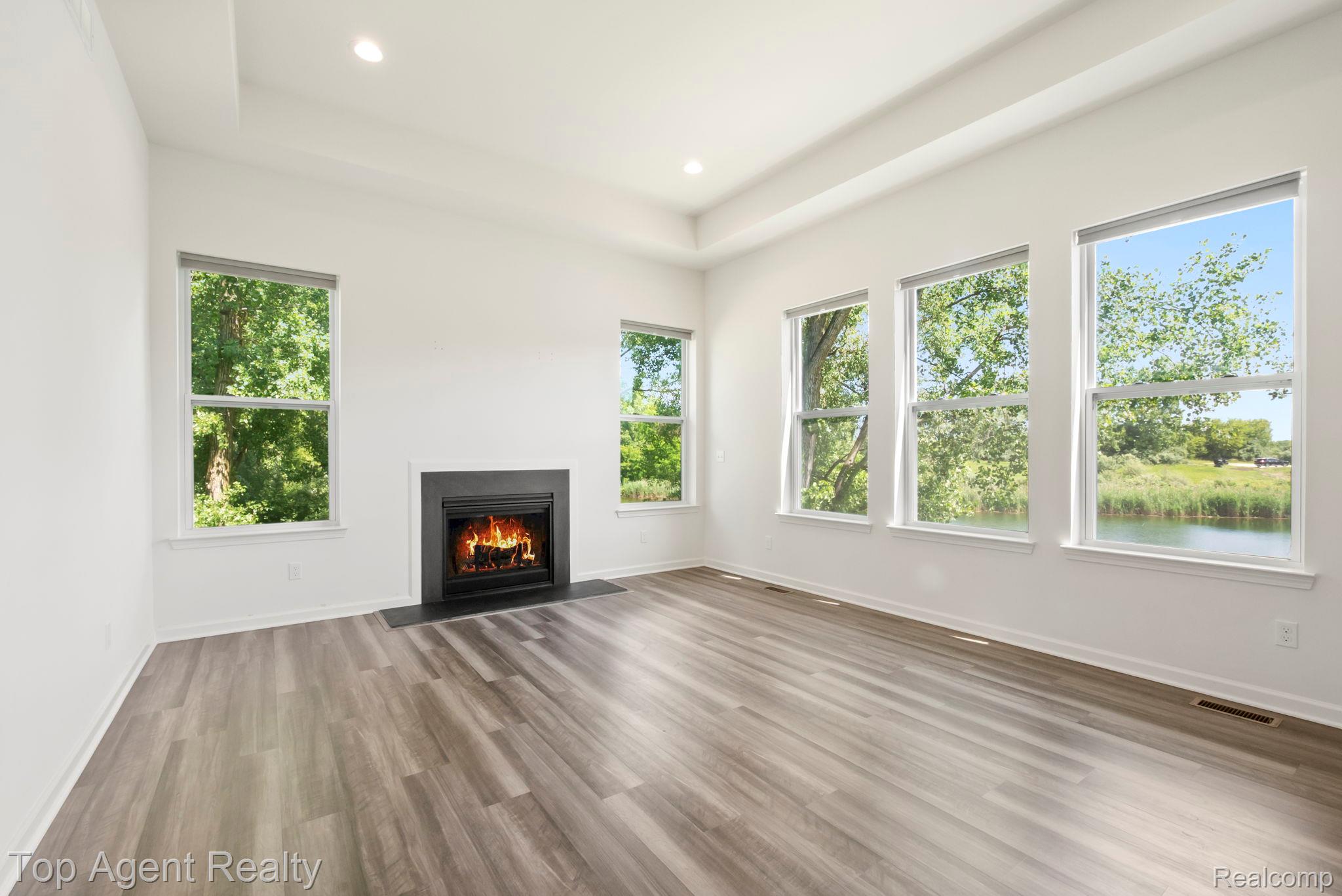 63770 Dequindre Road Washington, MI 48095 - Photo 2 of 61 Spacious room featuring a fireplace with a dark surround, multiple windows, wood-finish flooring, recessed lighting, and a tray ceiling