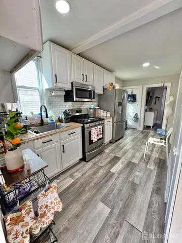 a kitchen with stainless steel appliances a stove a sink dishwasher a refrigerator white cabinets and wooden floor