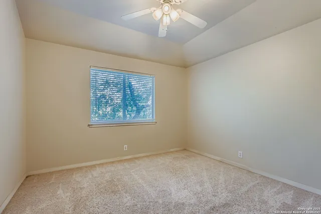 an empty room with a chandelier fan and windows