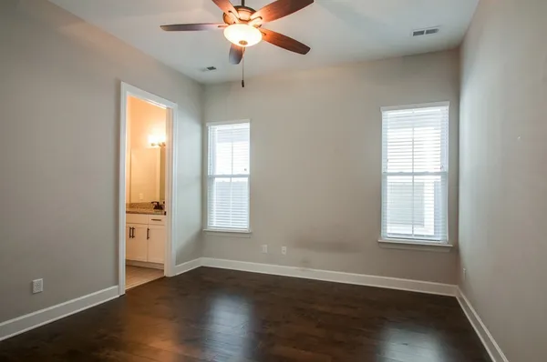 an empty room with wooden floor chandelier fan and windows