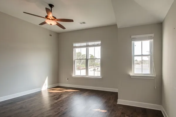 an empty room with wooden floor fan and windows