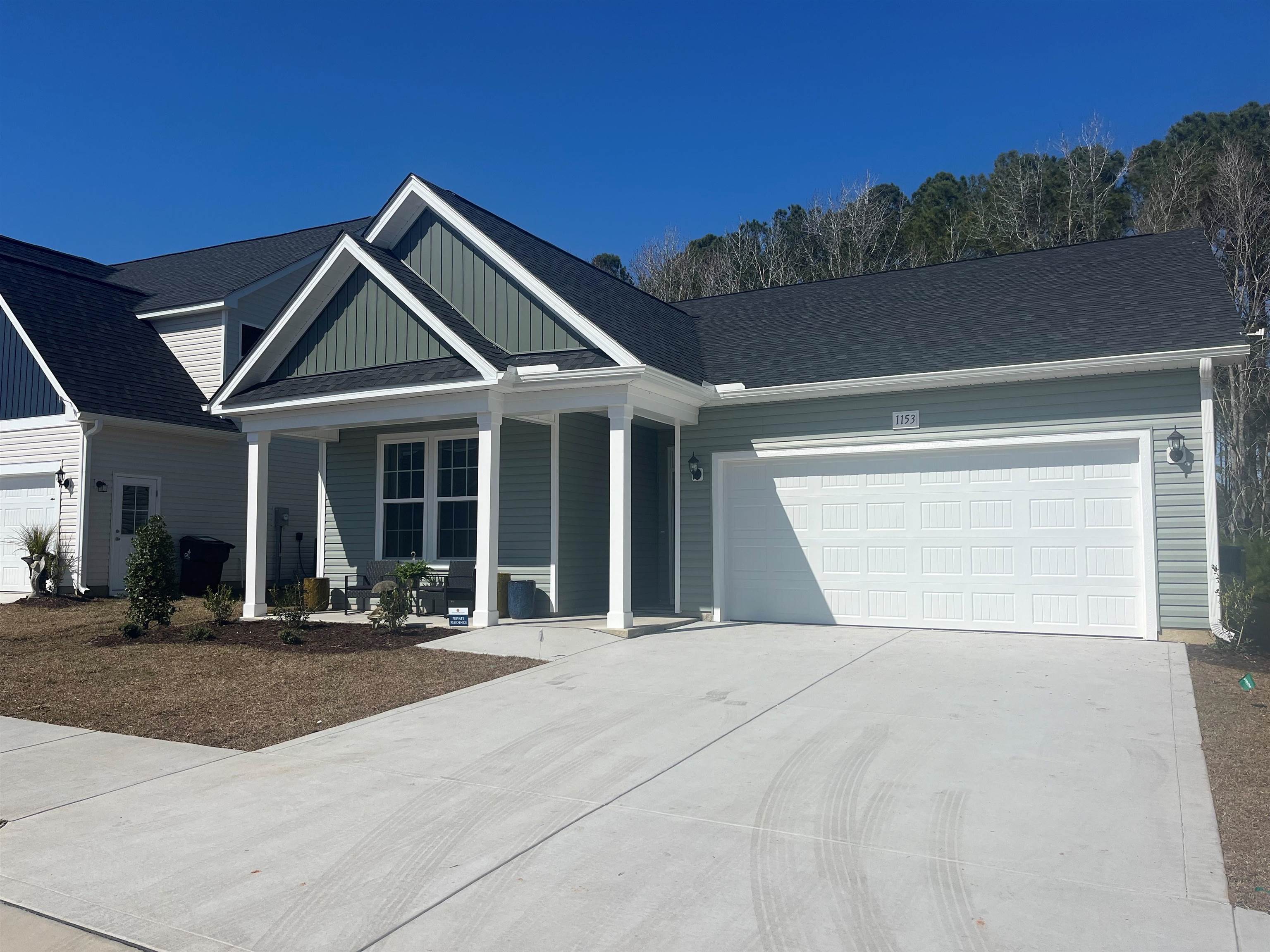 1053 Rosefield Way Calabash, NC 28467 - Photo 1 of 21 View of front of house featuring concrete driveway, board and batten siding, an attached garage, a shingled roof, and covered porch