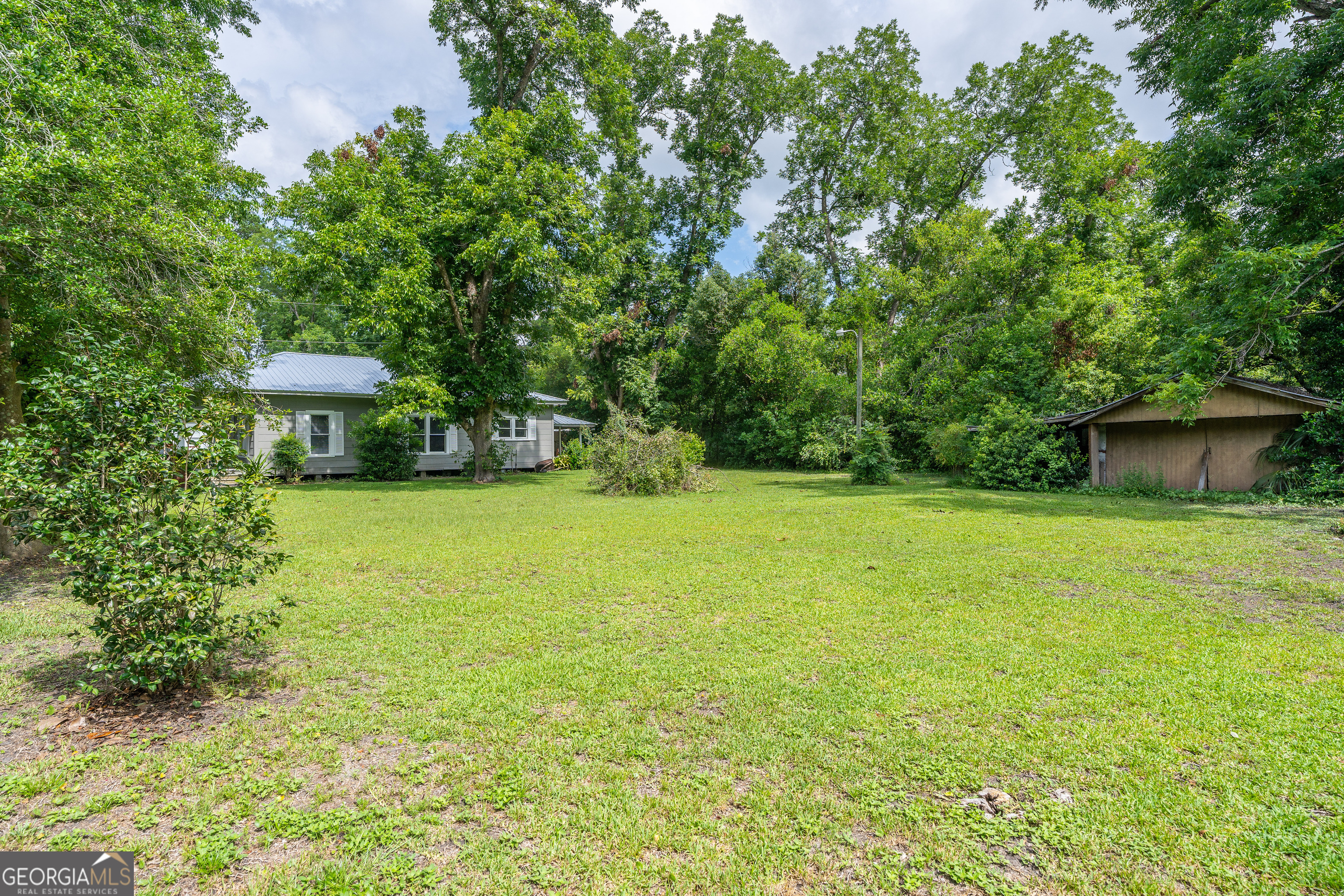 122 Hopkins Street Waycross, GA 31501 - Photo 11 of 31 a view of a garden with a bench and some plants and large trees