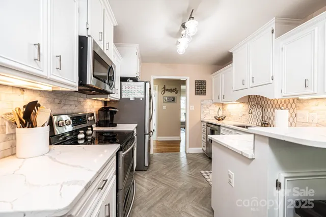 a kitchen with stainless steel appliances granite countertop a sink a stove a refrigerator and white cabinets
