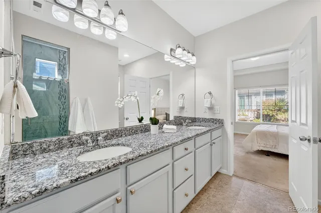 a spacious bathroom with a granite countertop double vanity sink a mirror a lamp a vanity and a bathtub