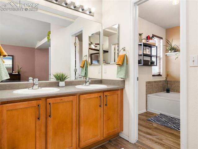 5346 Gentle Wind Road Colorado Springs, CO 80922 - Photo 23 of 28 Bathroom featuring double vanity, a sink, a garden tub, and wood finished floors