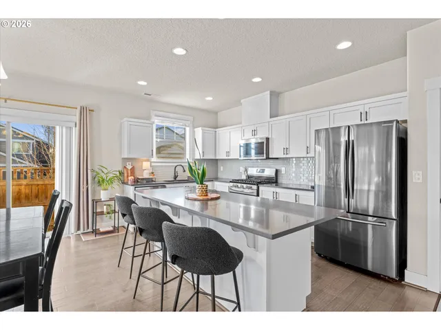 a kitchen with stainless steel appliances granite countertop a refrigerator a stove a sink a dining table and chairs