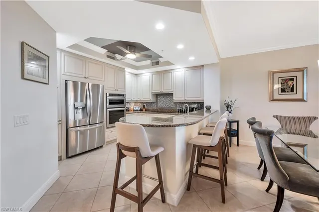 a kitchen with stainless steel appliances kitchen island granite countertop a dining table chairs refrigerator and sink