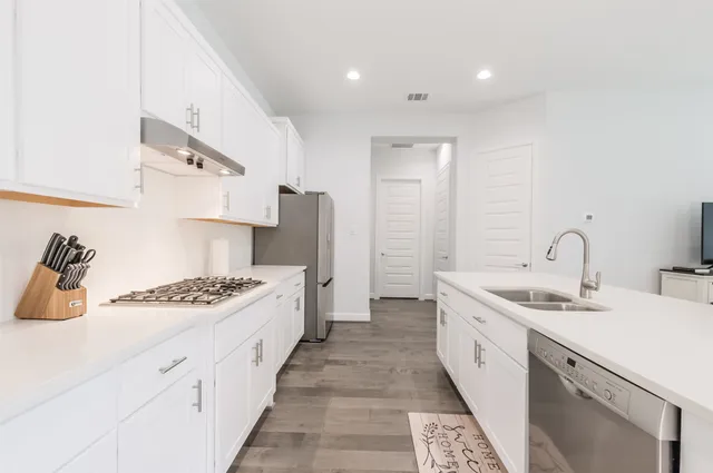 a kitchen with stainless steel appliances a sink dishwasher stove refrigerator and cabinets with wooden floor