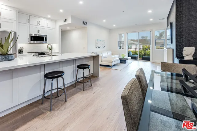 a large white kitchen with stainless steel appliances granite countertop a stove a sink a dining table and chairs