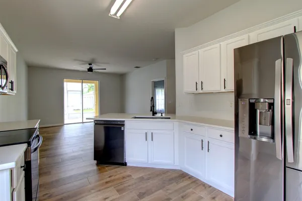 a kitchen with stainless steel appliances granite countertop a refrigerator a sink dishwasher a stove and white countertops with wooden floor