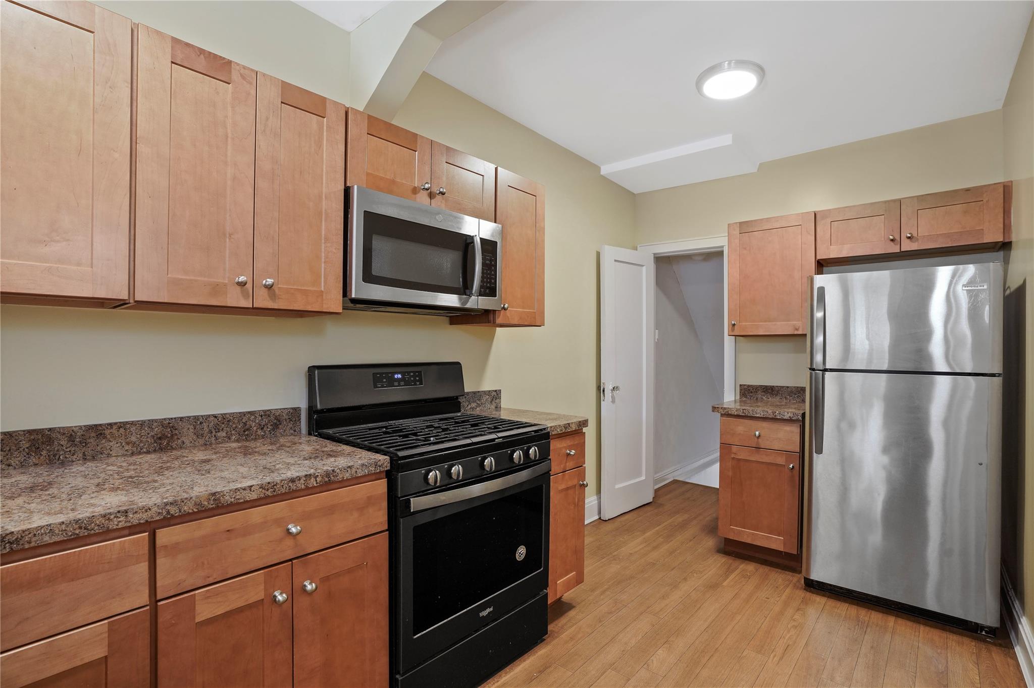 64-18 84th Place Queens, NY 11379 - Photo 12 of 35 a kitchen with granite countertop wooden cabinets stainless steel appliances and a wooden floor