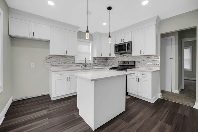 a kitchen with stainless steel appliances granite countertop a sink a microwave oven a refrigerator and white cabinets with wooden floor