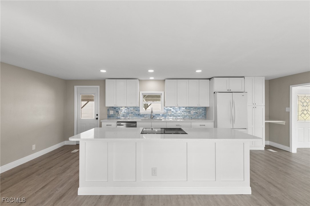 57 San Remo Circle Naples, FL 34112 - Photo 9 of 28 a kitchen with kitchen island sink stove and white cabinets with wooden floor