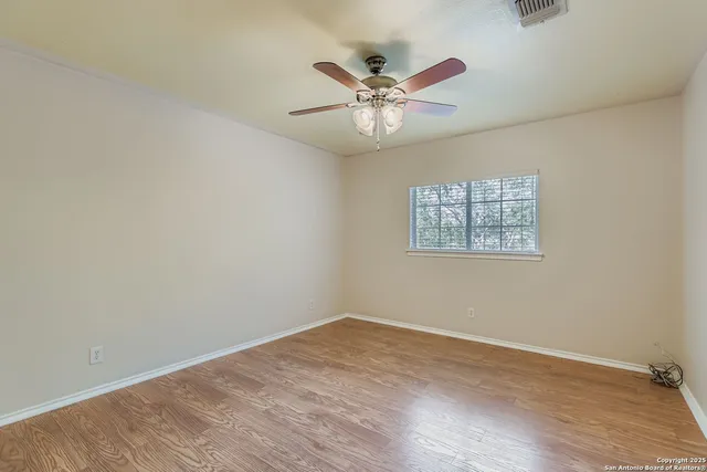 a view of an empty room with wooden floor and a chandelier fan