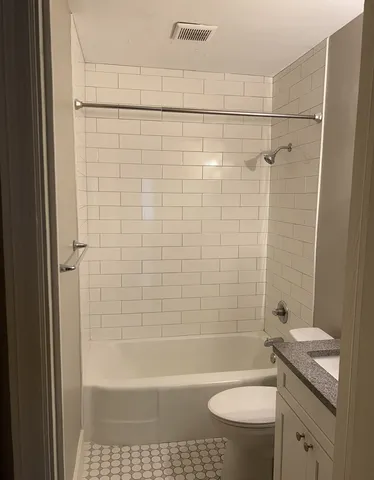 a bathroom with a granite countertop bathtub shower sink vanity and toilet