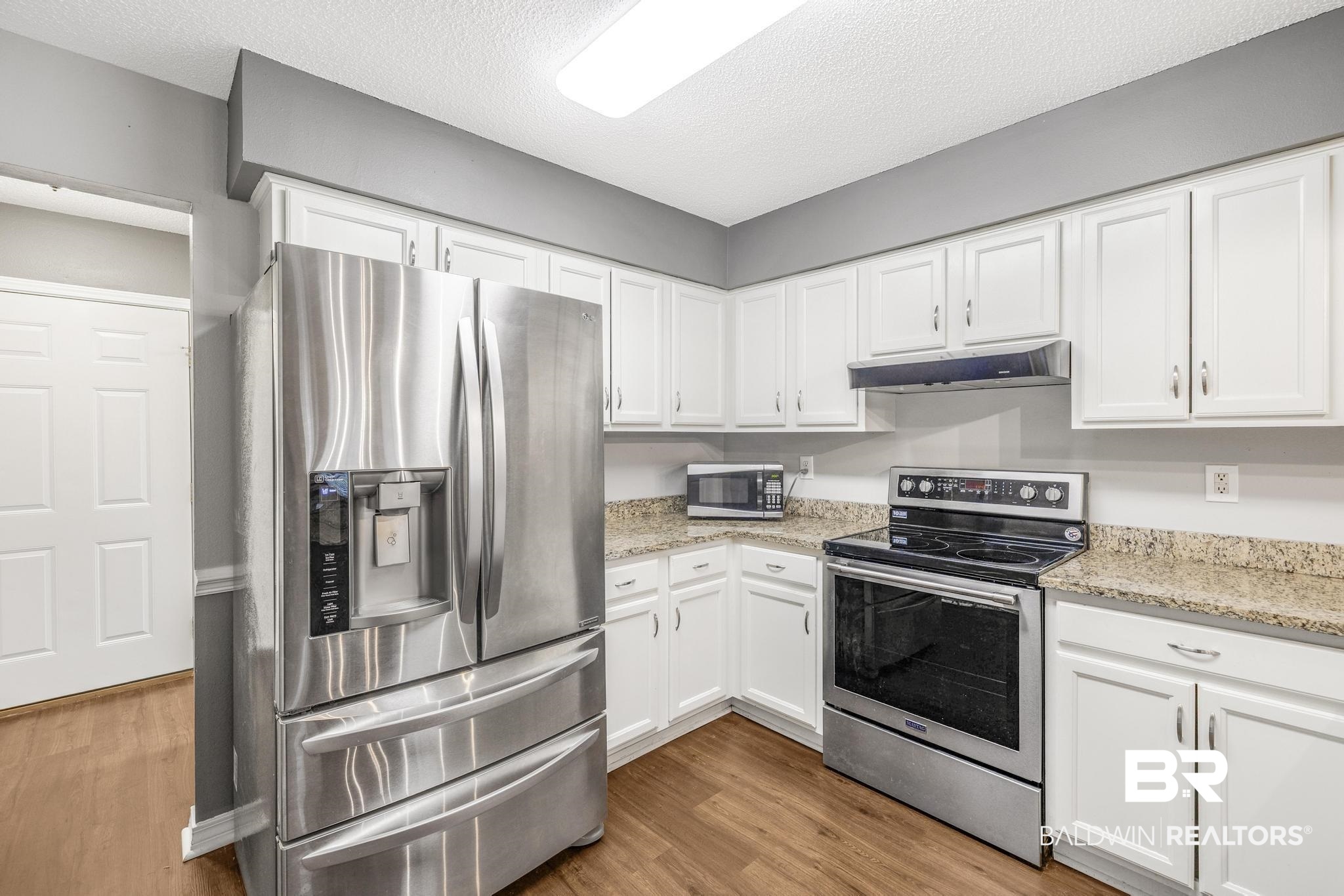140 Hope Drive Daphne, AL 36526 - Photo 12 of 54 Kitchen featuring stainless steel appliances, a textured ceiling, wood finished floors, white cabinets, and under cabinet range hood