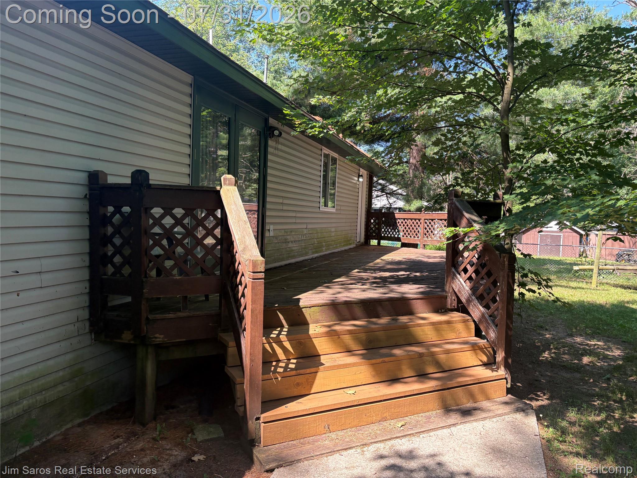 3871 Oakgrove Road Harrison, MI 48625 - Photo 4 of 12 Rear wood-finish deck with steps, lattice railing, and direct access to the interior via double glass doors