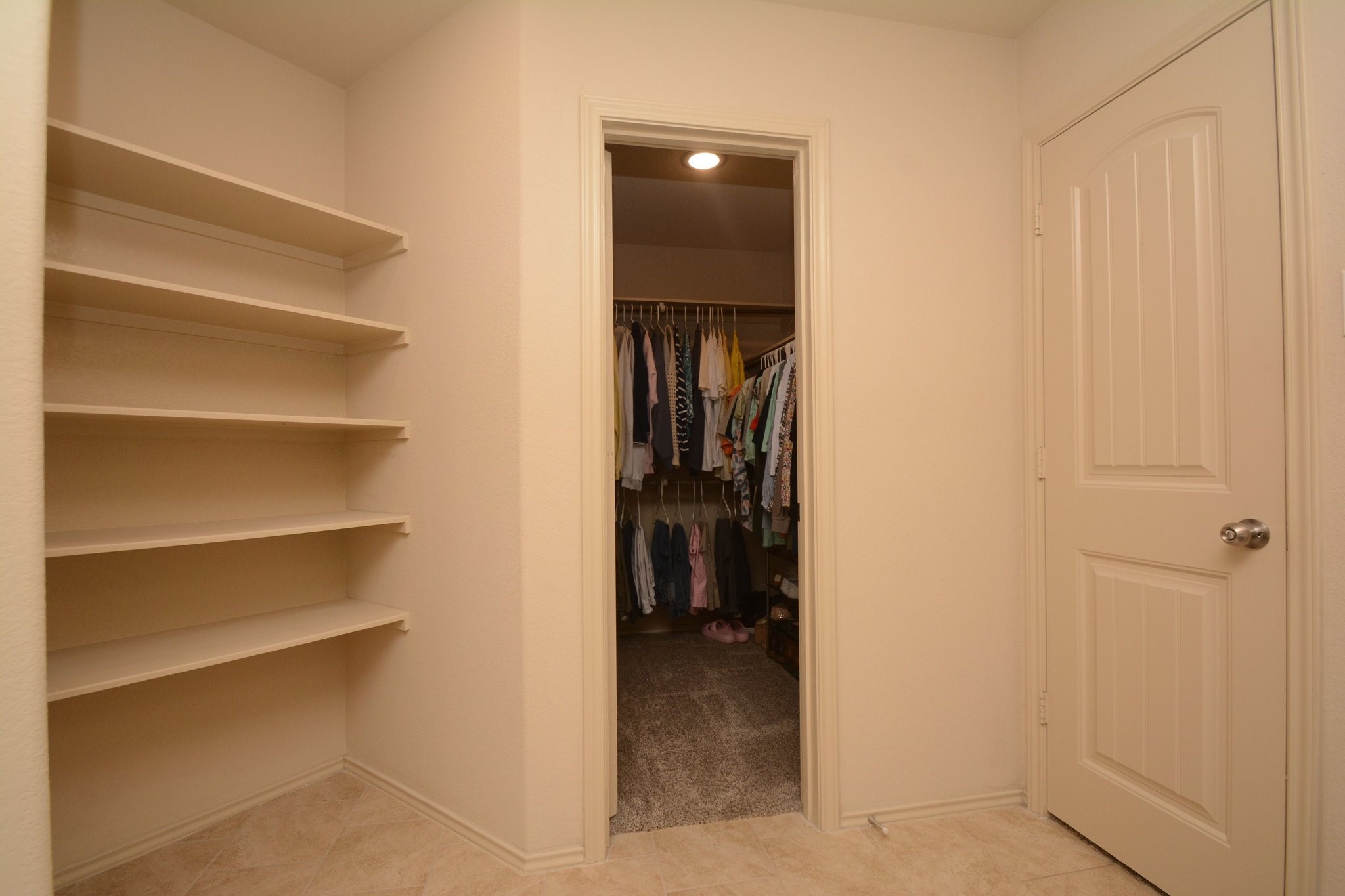 23318 Dukes Run Drive Spring, TX 77373 - Photo 32 of 41 This photo shows a walk-in closet with ample shelving on the left and a doorway leading to a clothes hanging area. The space is well-lit and has a neutral color scheme, offering plenty of storage.
