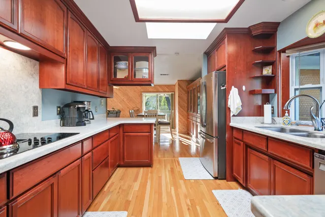 a kitchen with stainless steel appliances granite countertop a refrigerator a sink dishwasher and wooden cabinets with wooden floor