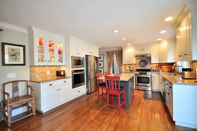 a kitchen with stainless steel appliances a refrigerator a stove top oven a sink dishwasher and white cabinets with wooden floor