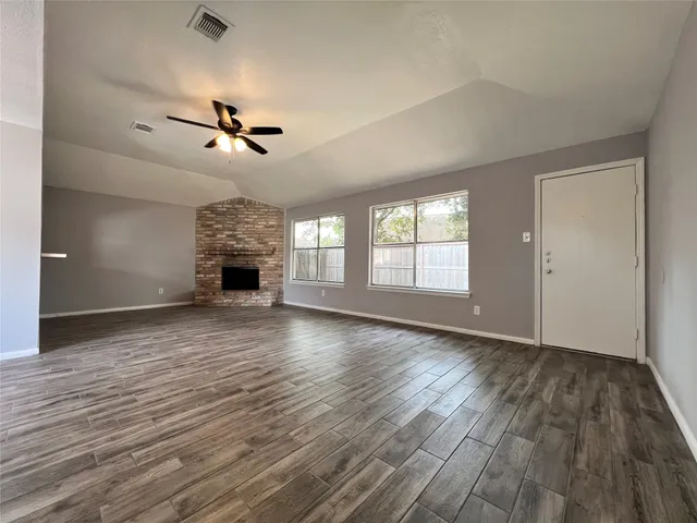 an empty room with wooden floor fireplace and windows