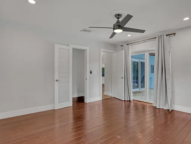 a view of an empty room with wooden floor and a ceiling fan