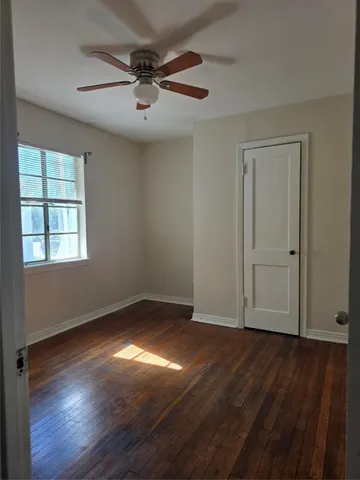 an empty room with wooden floor chandelier fan and windows