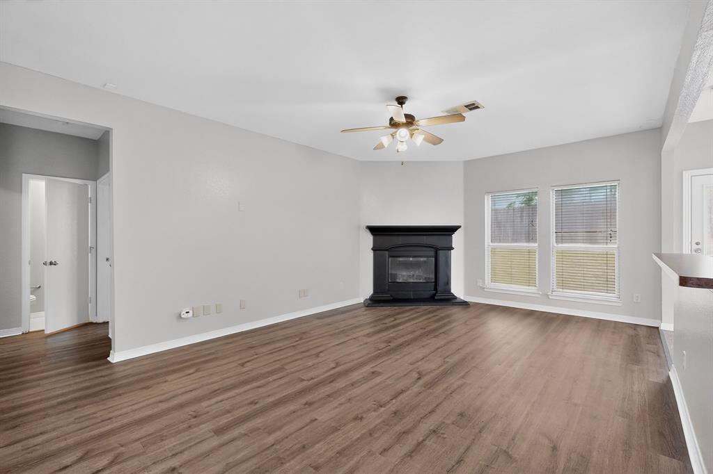 3401 Newgate Street Midlothian, TX 76065 - Photo 9 of 34 Spacious living area featuring wood-finish flooring, a corner fireplace with a black mantel, and a ceiling fan with integrated lighting