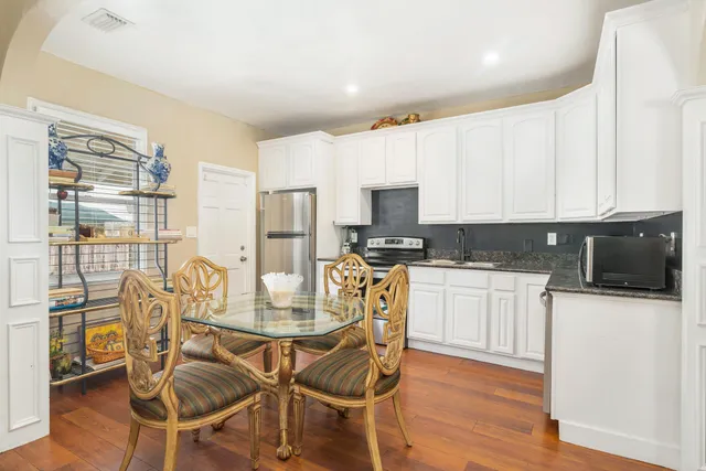 a kitchen with stainless steel appliances kitchen island granite countertop a refrigerator a stove top oven and white cabinets with wooden floor
