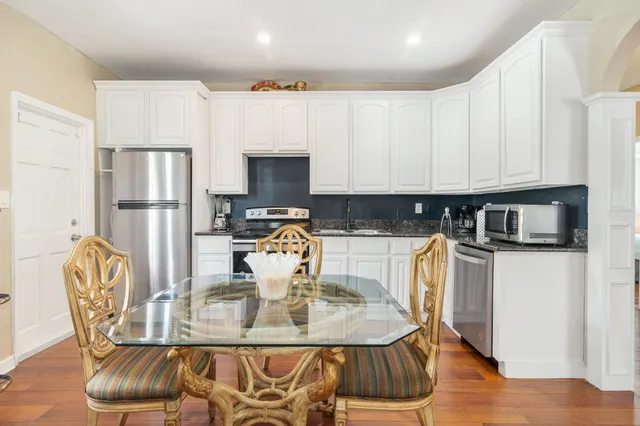 a kitchen with stainless steel appliances granite countertop a refrigerator a stove a sink dishwasher a dining table and chairs with wooden floor