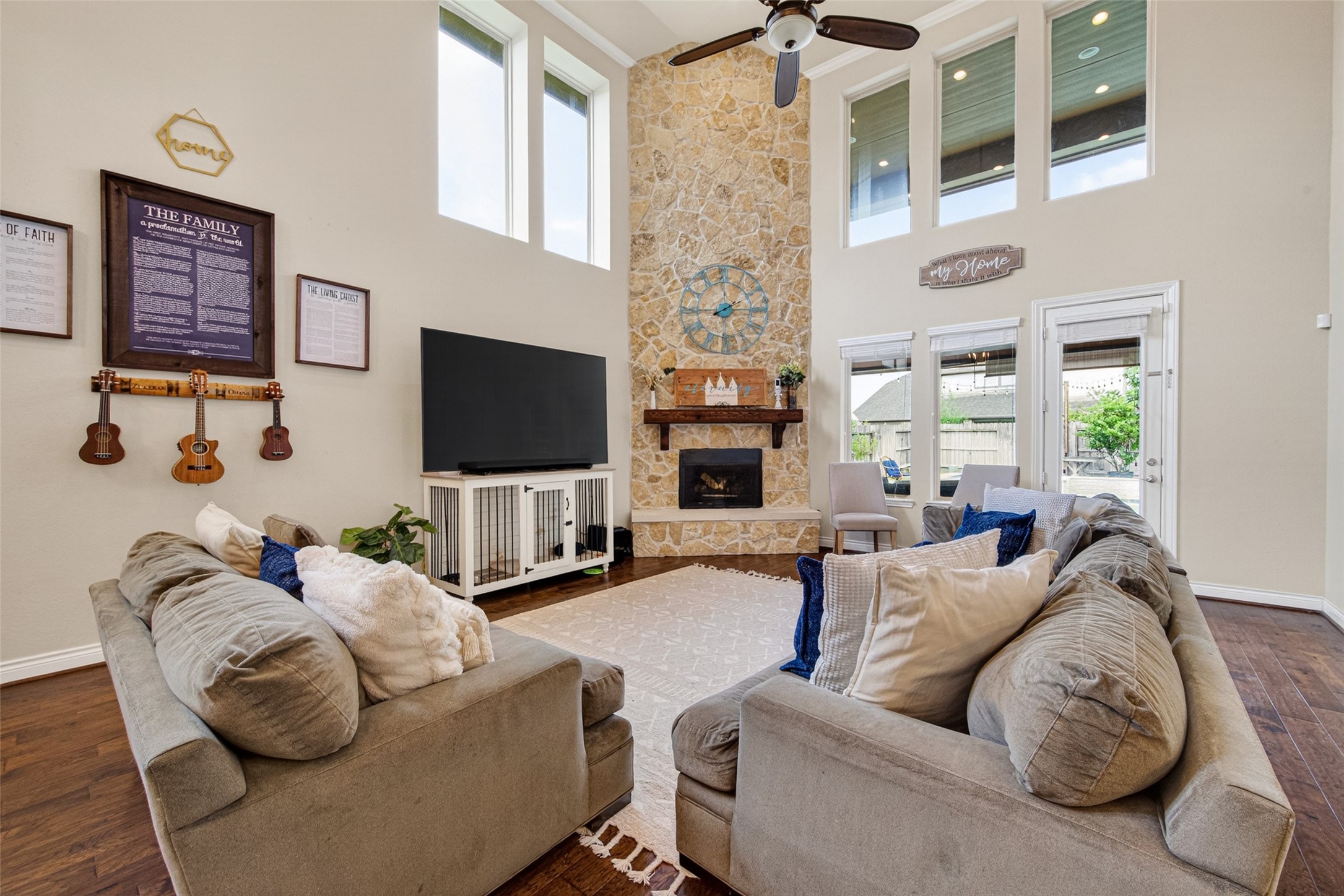 25611 Ellis Ridge Court Katy, TX 77494 - Photo 9 of 49 This spacious living room features high ceilings with large windows for natural light, a stone fireplace, and a cozy seating area. The open layout includes space for entertainment with a TV setup and access to a patio through glass doors.