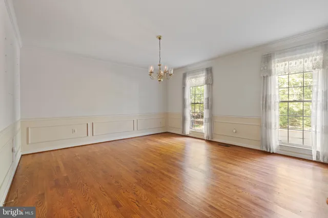 an empty room with wooden floor chandelier and windows