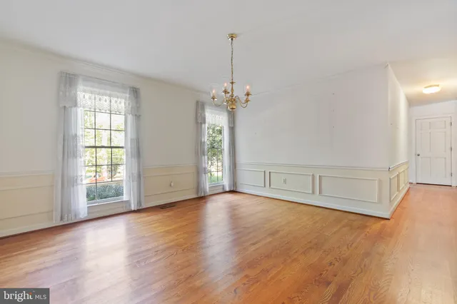 an empty room with wooden floor chandelier and windows