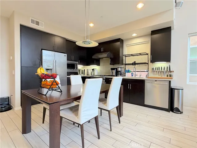 a kitchen with stainless steel appliances kitchen island granite countertop a dining table chairs refrigerator and sink