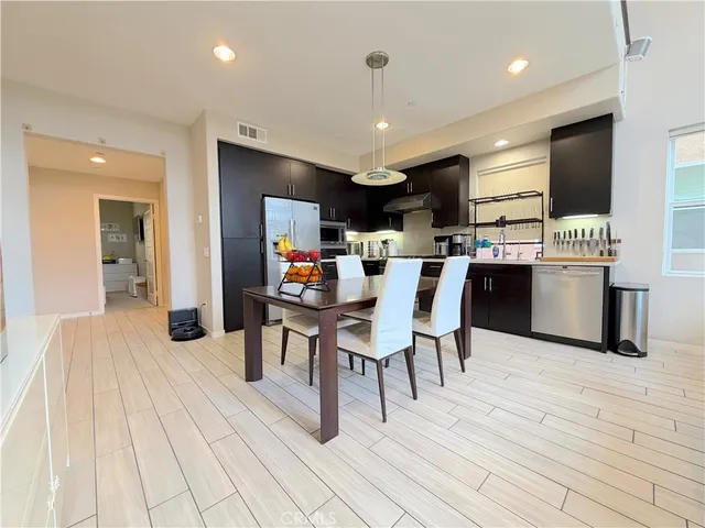 a dining hall with stainless steel appliances kitchen island granite countertop a table chairs and a sink