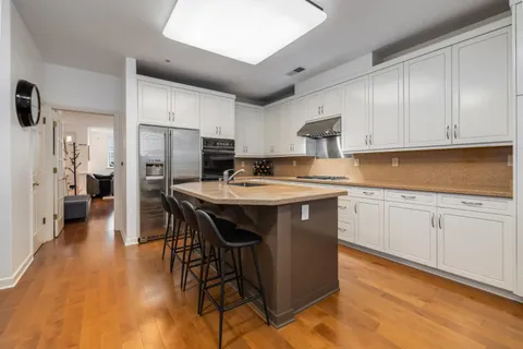 a kitchen with stainless steel appliances granite countertop a refrigerator a sink dishwasher a stove and white cabinets with wooden floor