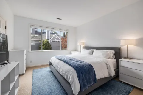 a bedroom with a large bed and a flat tv screen on dresser next to a window
