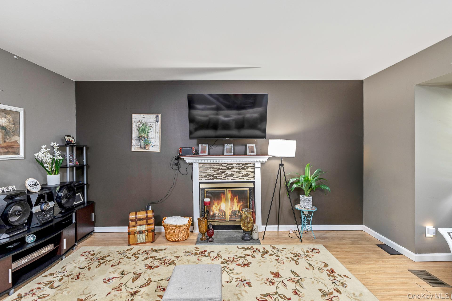17 Stone Commons Yaphank, NY 11980 - Photo 9 of 31 Living area featuring wood-finish flooring, a fireplace with a stacked stone facade and white mantel, and a dark accent wall