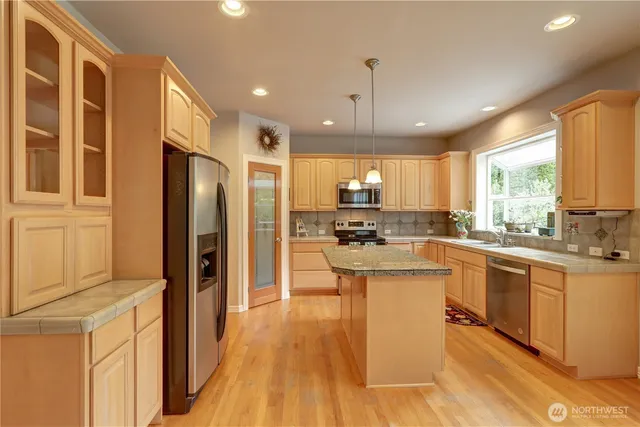 a kitchen with stainless steel appliances granite countertop a refrigerator a sink dishwasher a stove and white countertops with wooden floor