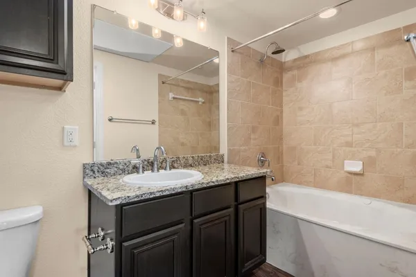 a bathroom with a granite countertop sink a toilet a mirror and shower