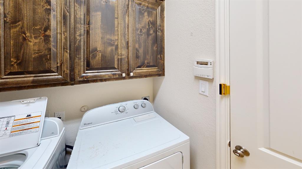14712 Spitfire Trail Fort Worth, TX 76262 - Photo 8 of 25 Laundry area featuring dark wood-finish cabinetry, white textured walls, and a light-colored door with a brass hinge