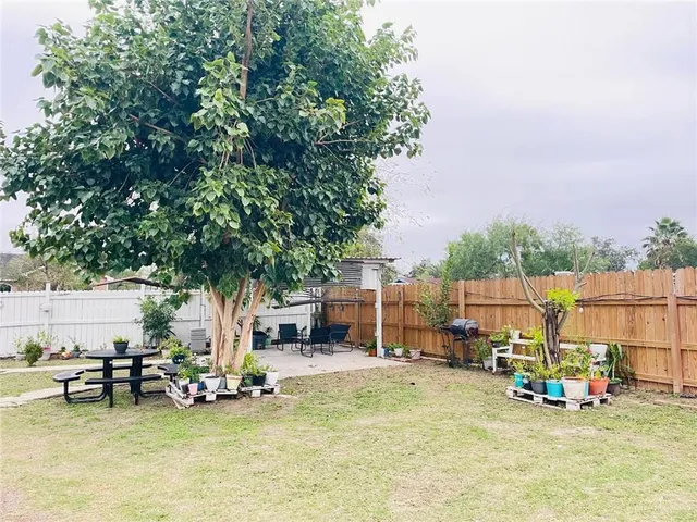 a view of a backyard with table and chairs and a barbeque with potted plants and large tree