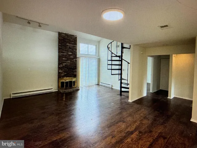 an empty room with wooden floor staircase and windows