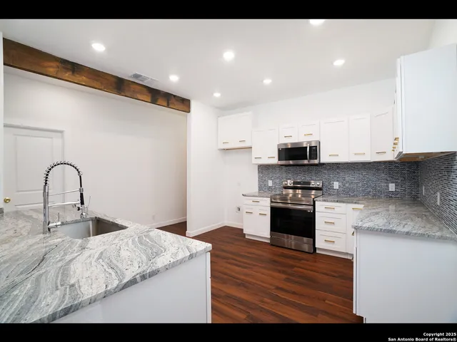 a kitchen with stainless steel appliances granite countertop a stove top oven a sink and white cabinets