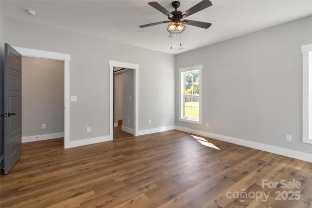 an empty room with wooden floor chandelier fan and windows