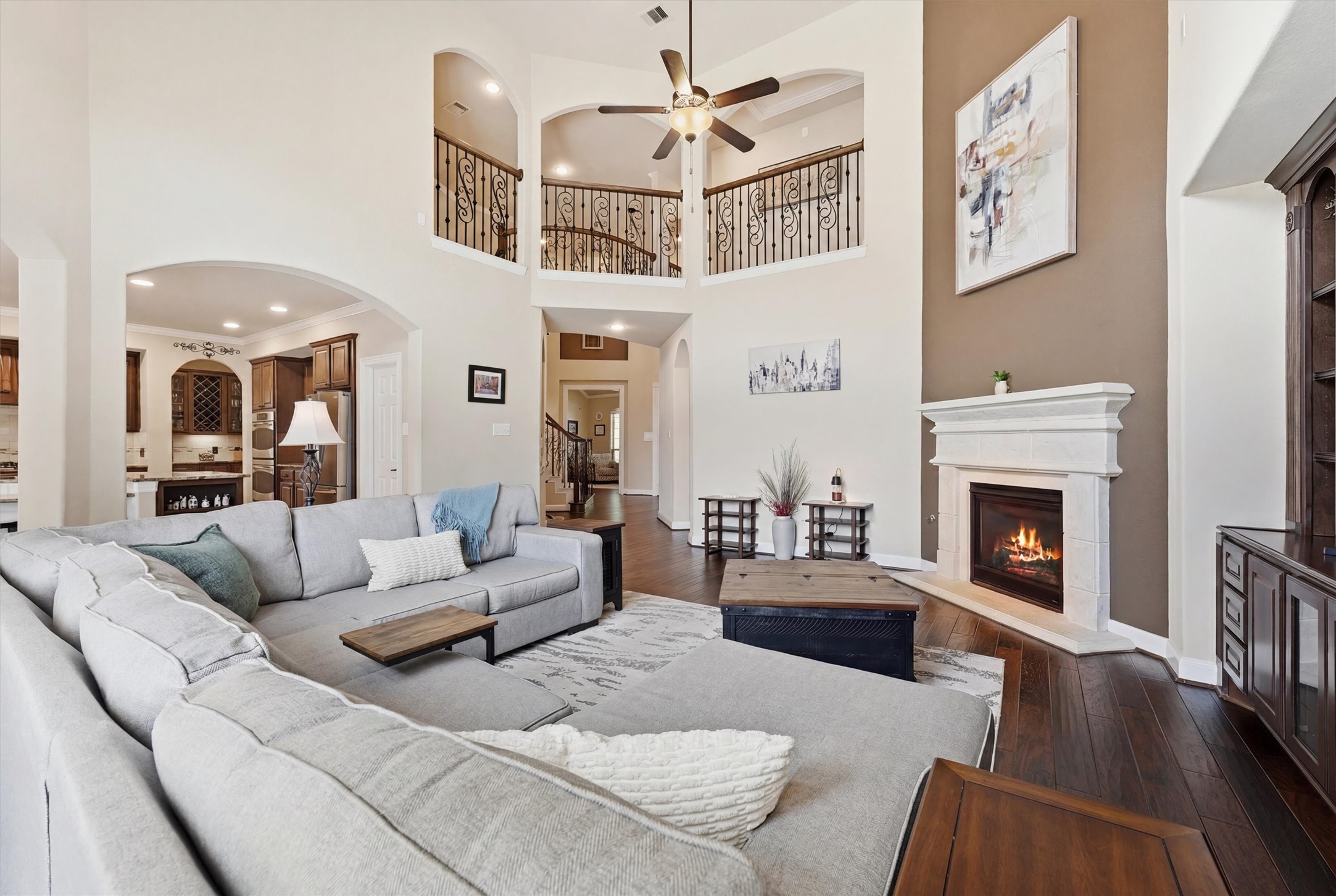 17710 Rough River Court Humble, TX 77346 - Photo 11 of 38 This spacious living room features a cozy fireplace, high ceilings with a ceiling fan, a large sectional sofa, and elegant wood flooring. The open layout connects to the kitchen, and an upstairs balcony adds a touch of sophistication.