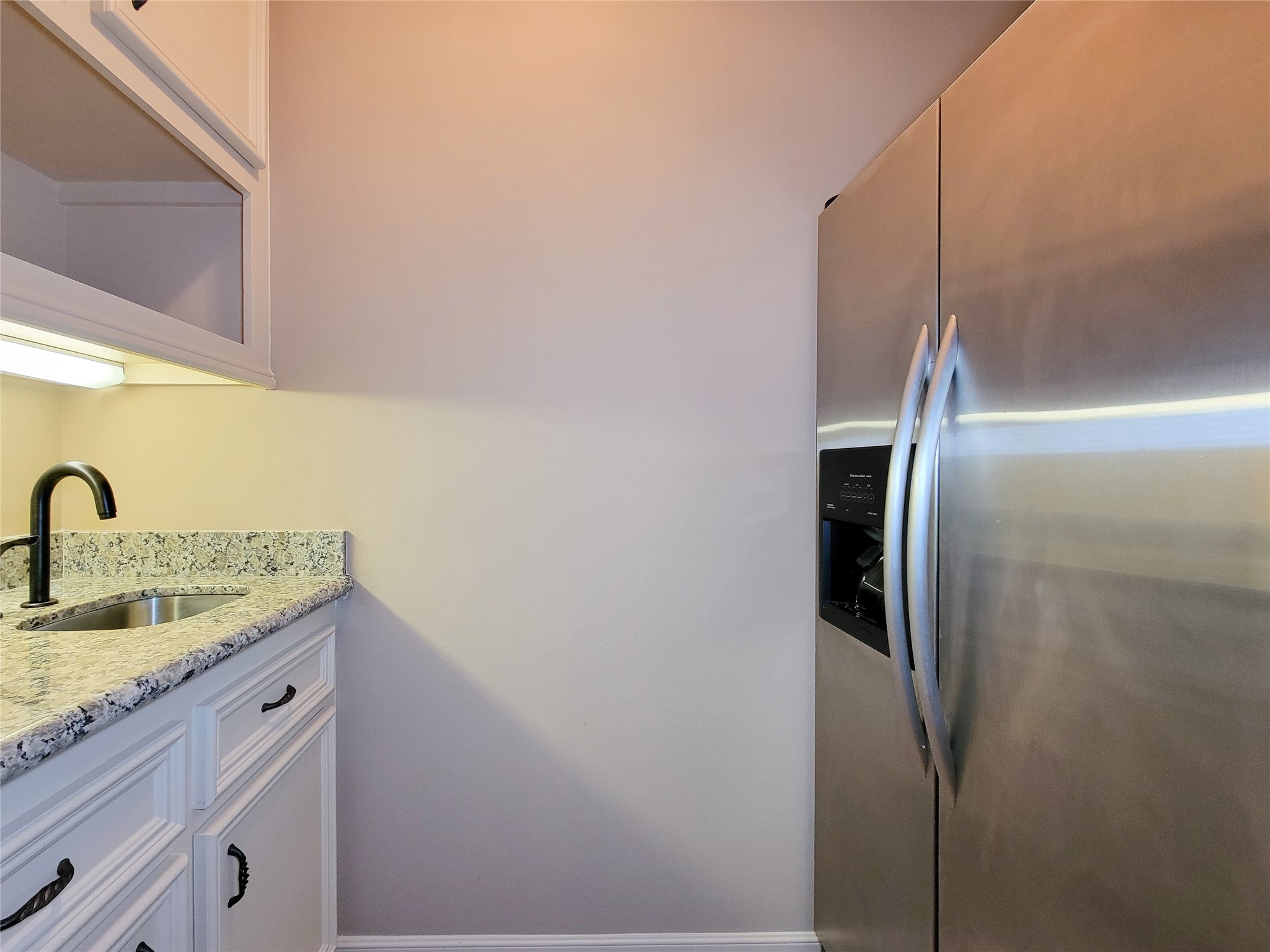 1118 Colonial Street Bellaire, TX 77401 - Photo 33 of 50 This photo shows the media room kitchen area with a granite countertop, a stainless steel sink, and a side-by-side stainless steel refrigerator. There are upper cabinets for storage and modern fixtures.