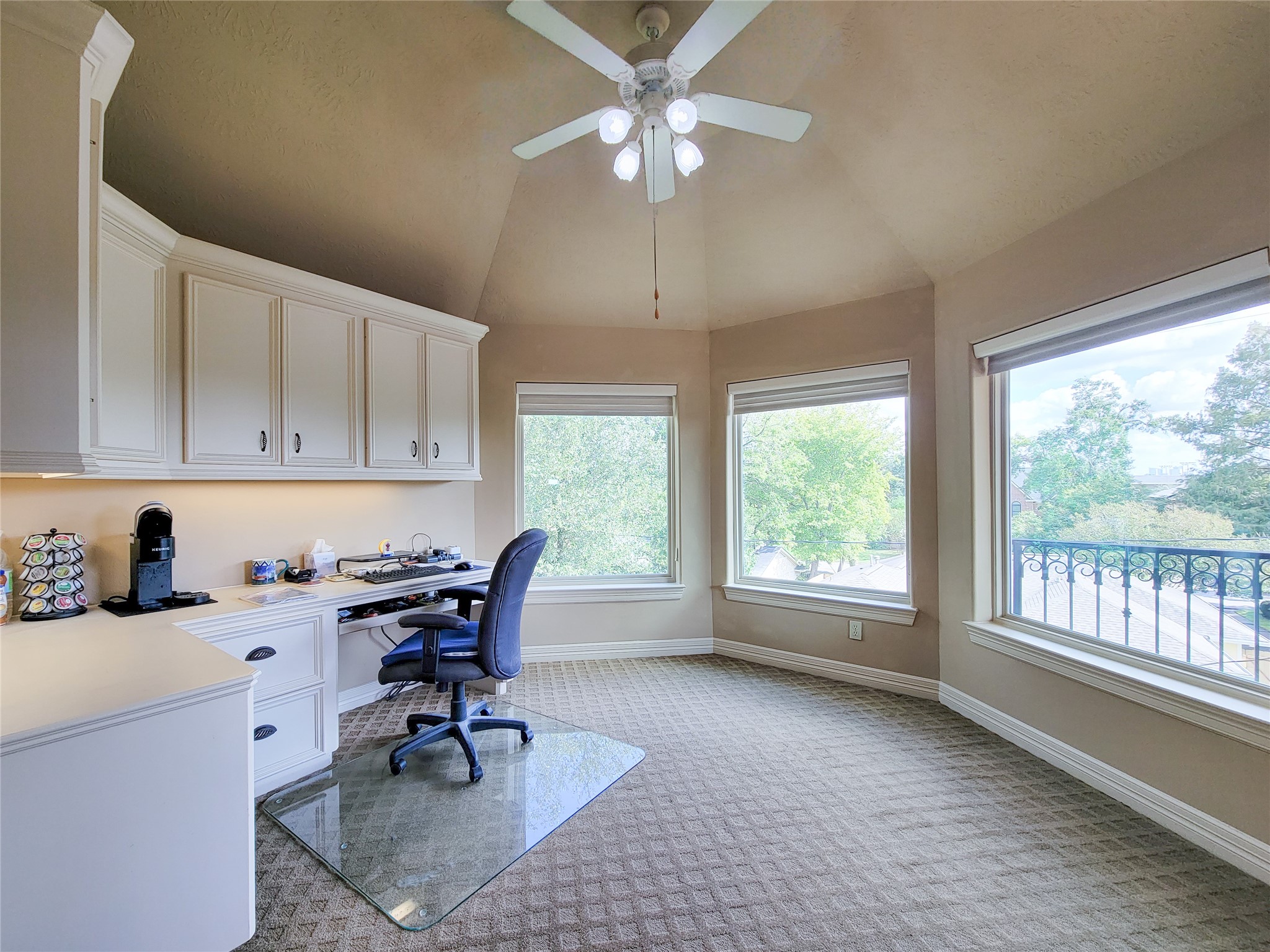 1118 Colonial Street Bellaire, TX 77401 - Photo 36 of 50 This fifth bedroom features large windows offering abundant natural light and scenic views. It includes built-in cabinets for storage, a spacious desk area, and a ceiling fan for comfort. The room has a neutral color palette and carpeted flooring.
