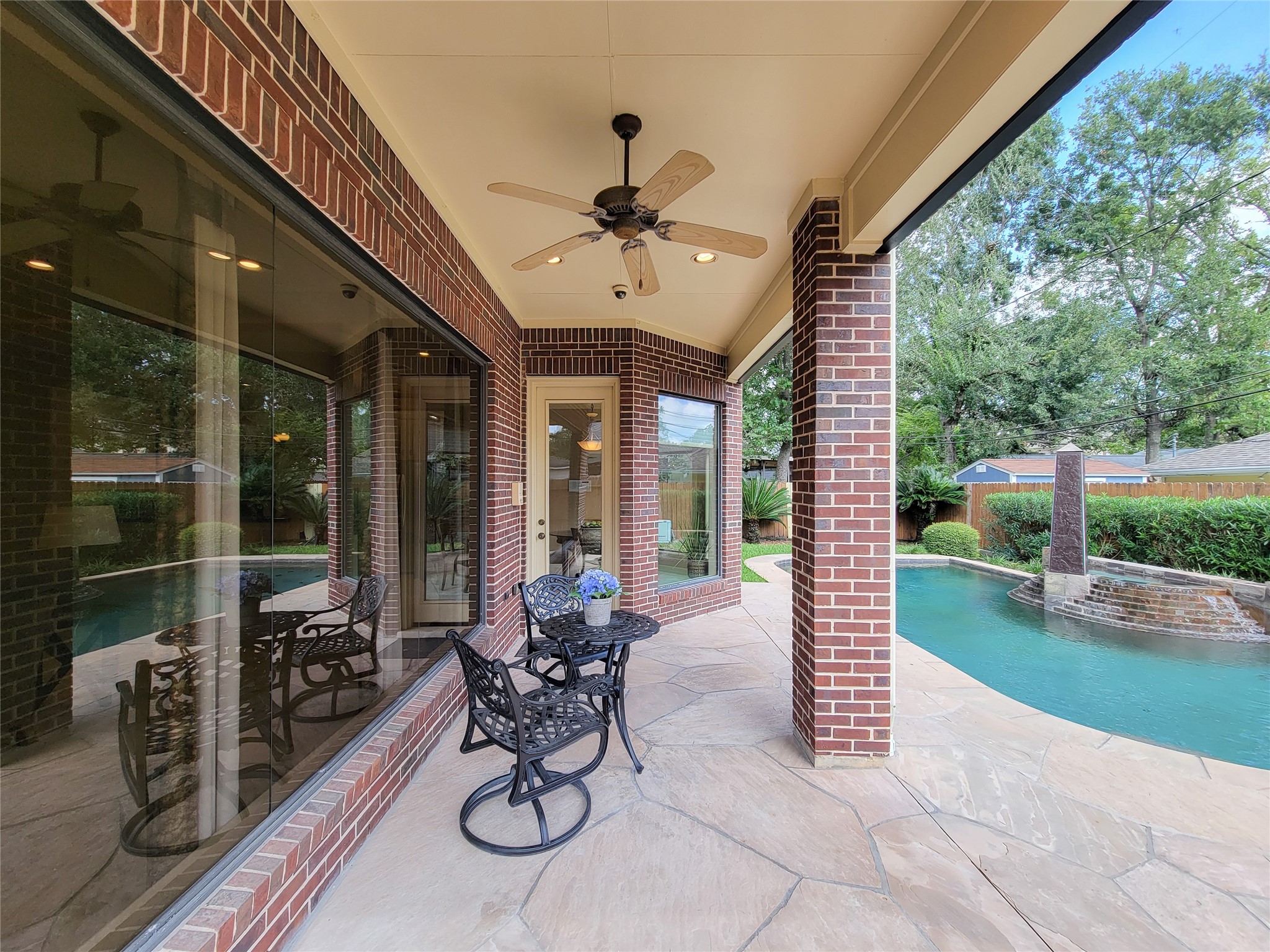 1118 Colonial Street Bellaire, TX 77401 - Photo 38 of 50 This photo showcases a charming covered patio with a ceiling fan and elegant brick columns. It overlooks a serene pool and landscaped backyard, offering a perfect setting for relaxation and outdoor entertaining.